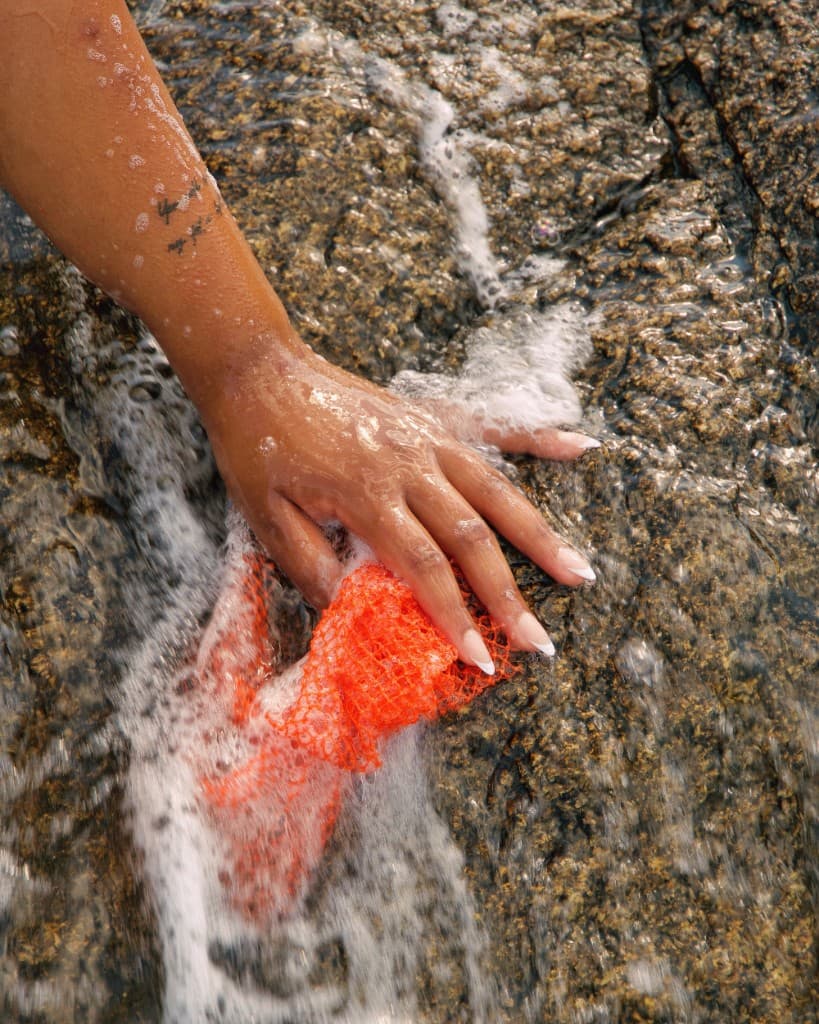 A hand pressing a red mesh into sea foam on dark rock